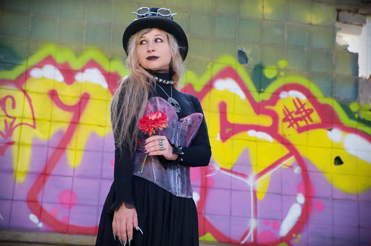 Stylish woman in gothic attire posing against a vibrant graffiti wall.