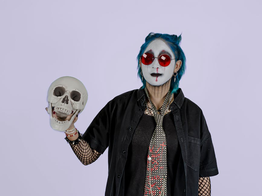 Person in gothic makeup and red sunglasses holding a skull against a soft purple background.