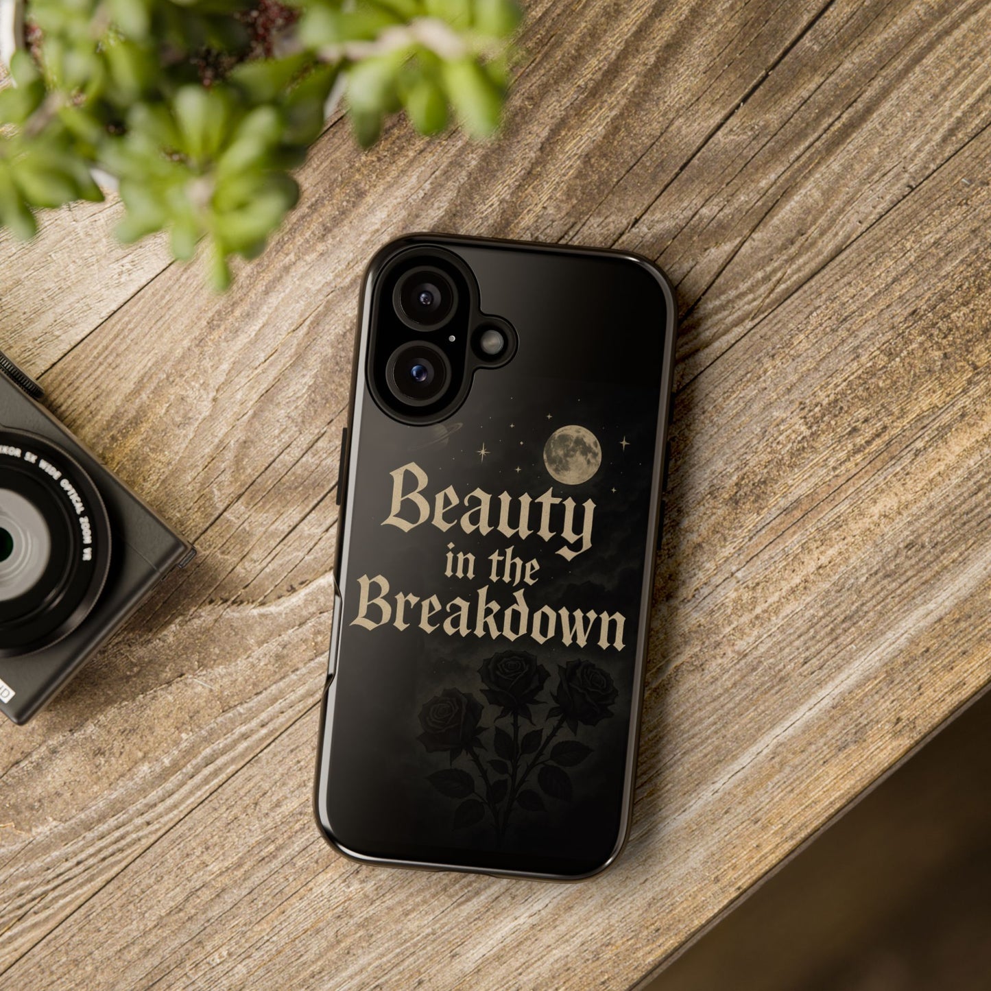 Phone case with 'Beauty in the Breakdown' text on a wooden surface with a camera and plant.