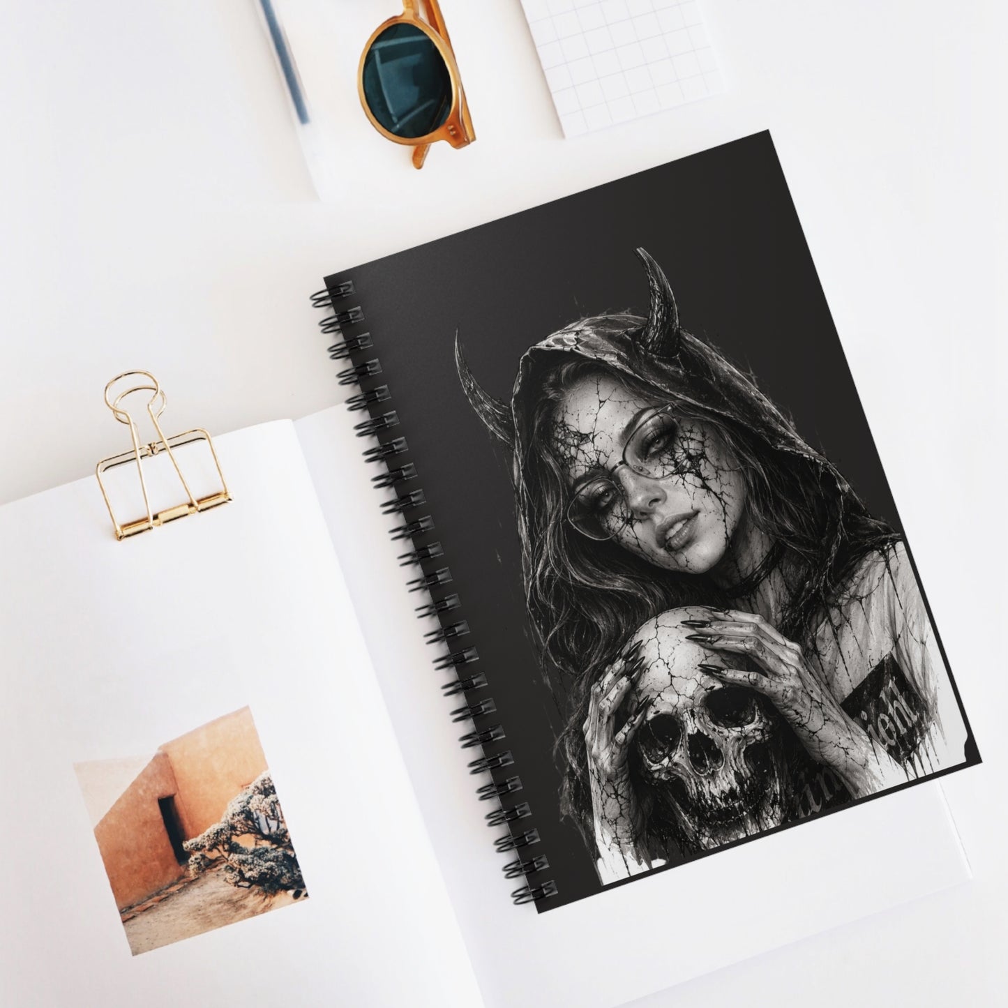 Notebook with a black and white illustration of a hooded figure holding a skull on a white surface.