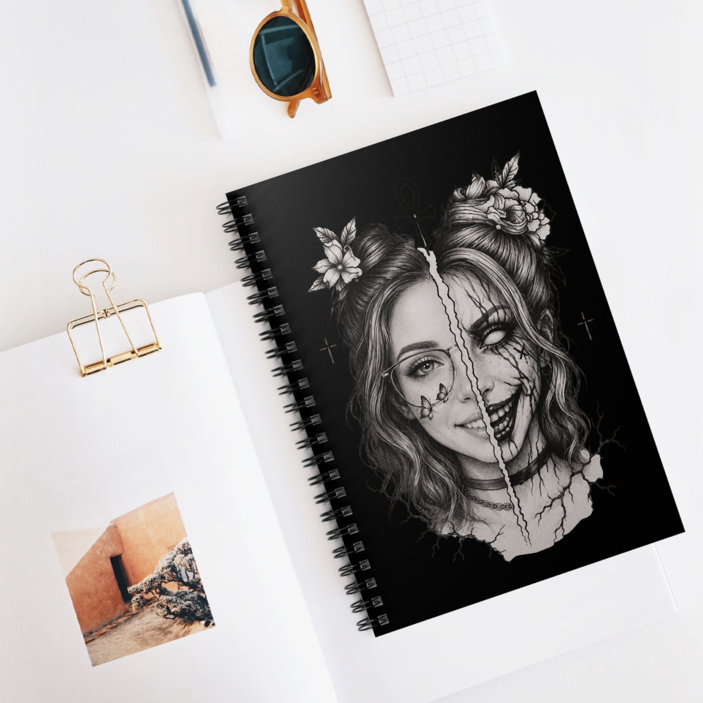 Spiral-bound notebook with a black and white illustration of a woman's face on a white surface.