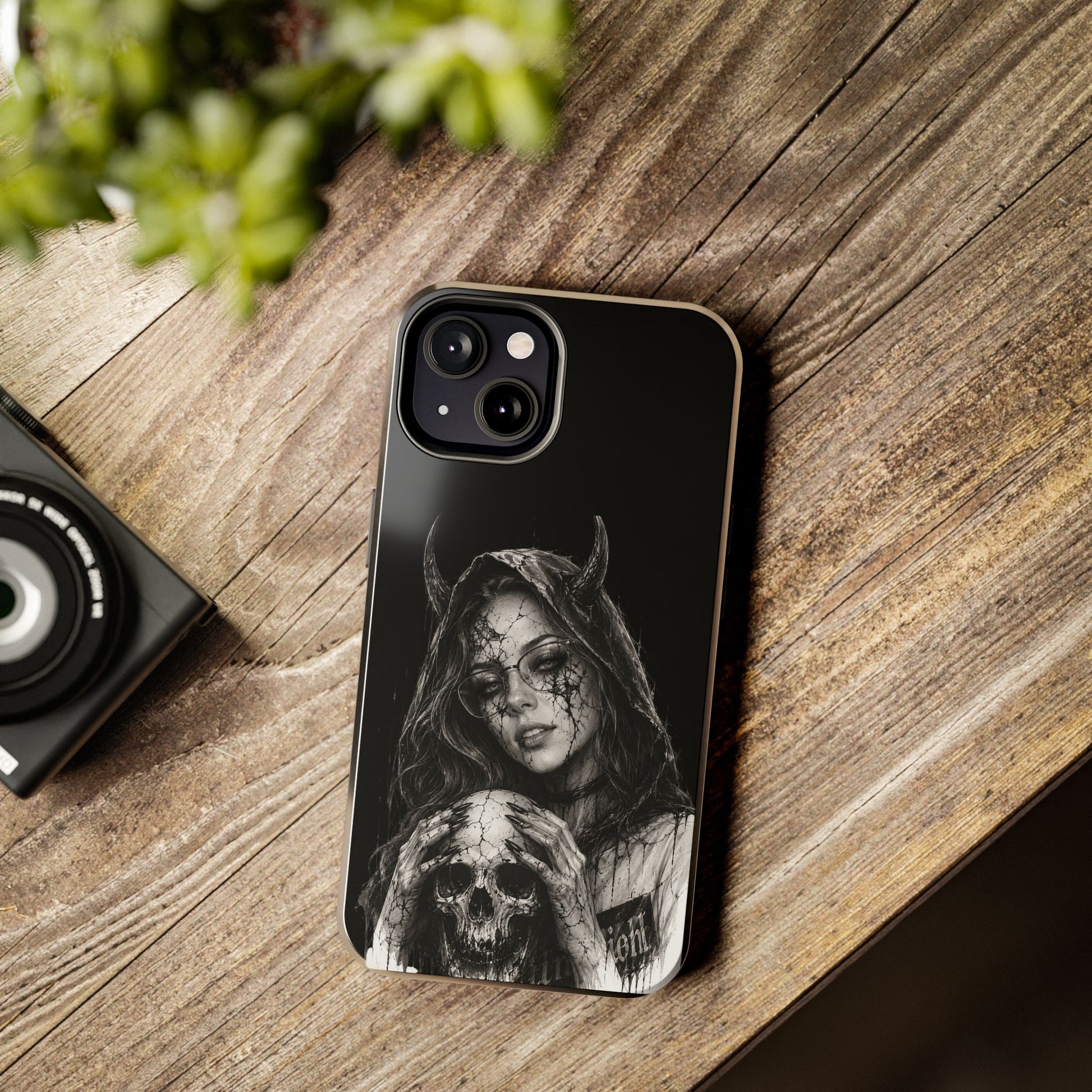 Phone case with a black and white design of a hooded figure and skull on a wooden surface.